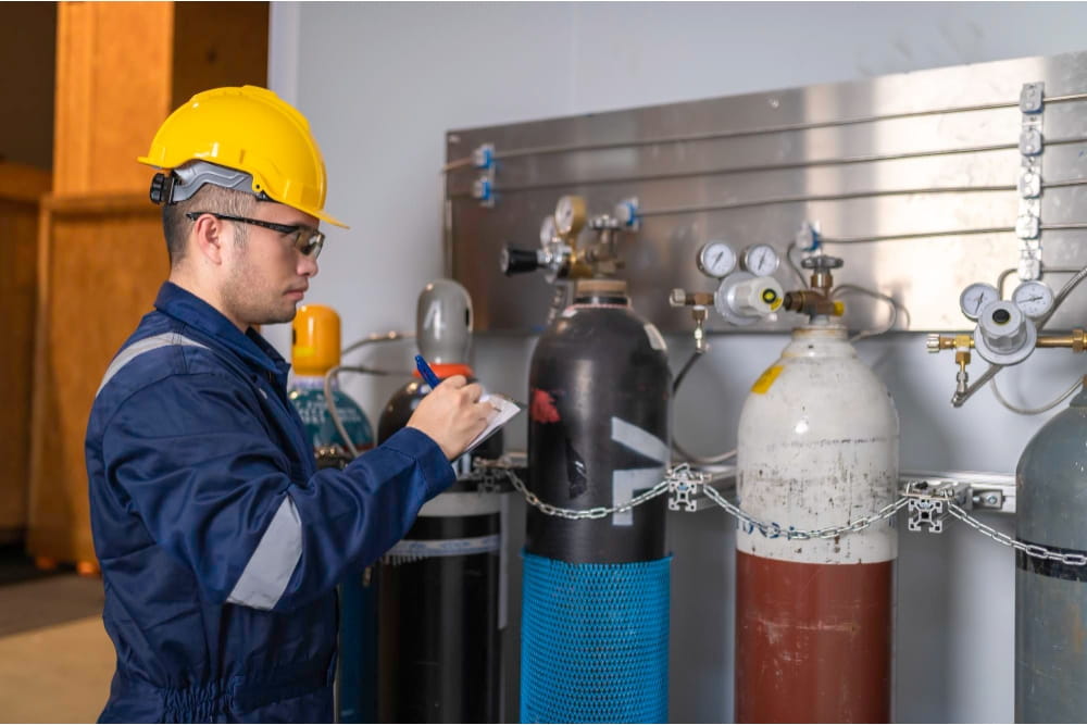 Gas engineer in blue coveralls inspects industrial gas cylinders and pressure gauges