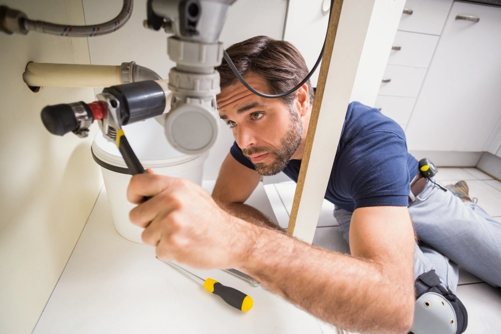 NVQ Level 2 Plumbing Diploma student or professional plumber working on kitchen sink pipework with a wrench